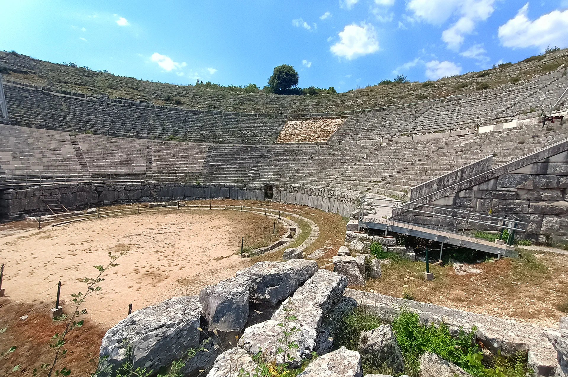 Stone seating and stage area of the ancient theater of Dodona, set against a green hillside in Epirus, Greece.