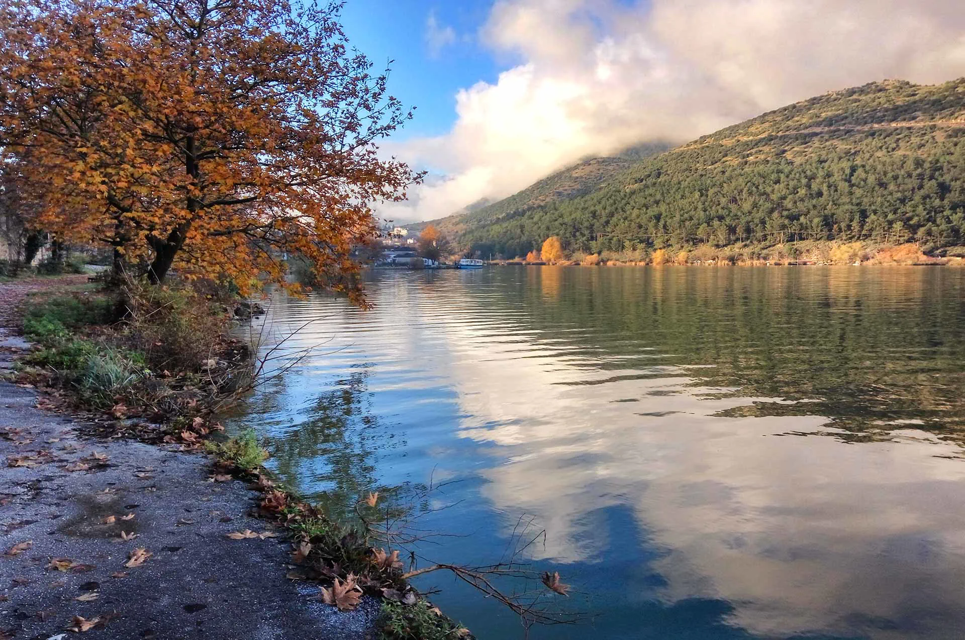 Tranquil view of Lake Pamvotida in Ioannina with reflections of the mountains and the island in the distance.