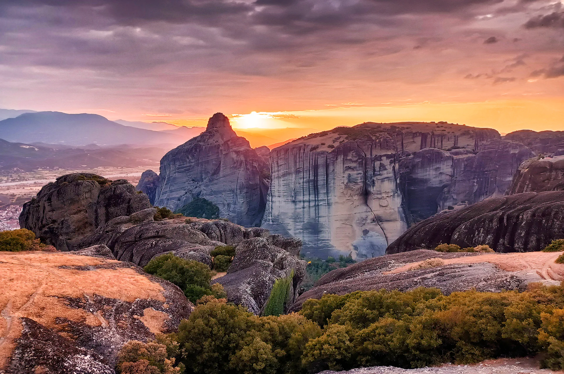 Sunset over the Meteora cliffs with ancient buildings silhouetted.
